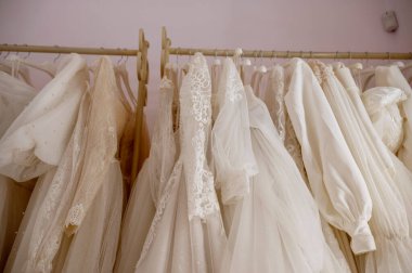 Gelinlik salonunda askıdaki beyaz gelinlikler. Gelinlik salonundaki ağırlıklı beyaz arka plana karşı uzun bir gelinlik askısı.