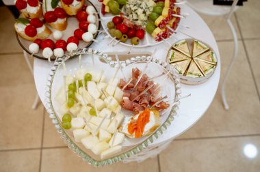 Renkli bir tabak doğranmış beyaz peynir ve üzüm, zarif bir şekilde dekoratif kürdanlı cam bir tabakta. Güzel sunulmuş bir sandviç tabağı taze ekmek, kiraz domatesleri, zeytinler.