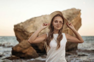 Yazlık şapkalı genç, narin bir kadın deniz kıyısında yalınayak yürüyor. Uzun saçlı, beyaz elbiseli bir sarışın kumsalda geziniyor. Deniz kıyısında gezmekten hoşlanıyor.
