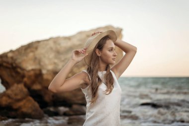 Yazlık şapkalı genç, narin bir kadın deniz kıyısında yalınayak yürüyor. Uzun saçlı, beyaz elbiseli bir sarışın kumsalda geziniyor. Deniz kıyısında gezmekten hoşlanıyor.