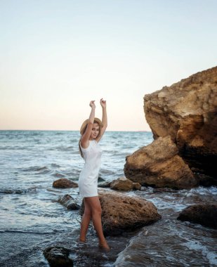 Yazlık şapkalı genç, narin bir kadın deniz kıyısında yalınayak yürüyor. Uzun saçlı, beyaz elbiseli bir sarışın kumsalda geziniyor. Deniz kıyısında gezmekten hoşlanıyor.