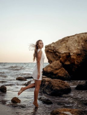 Yazlık şapkalı genç, narin bir kadın deniz kıyısında yalınayak yürüyor. Uzun saçlı, beyaz elbiseli bir sarışın kumsalda geziniyor. Deniz kıyısında gezmekten hoşlanıyor.