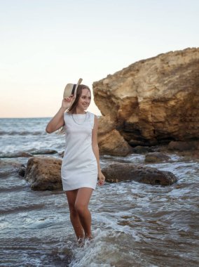 Yazlık şapkalı genç, narin bir kadın deniz kıyısında yalınayak yürüyor. Uzun saçlı, beyaz elbiseli bir sarışın kumsalda geziniyor. Deniz kıyısında gezmekten hoşlanıyor.