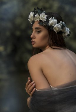 Omuzlarının üzerinde beyaz bir gül çelengi ve bir orman gölü yakınında gri bir peçeyle genç bir bayanın romantik portresi. Manevi güzellik, fantezi estetiği ve sessiz yalnızlık kavramı..