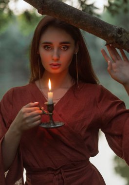 Yüzü sıcak mum alevi tarafından vurgulanmış çarpıcı bir kızın yakın plan portresi. Doğal güzellik kavramı, sıcaklık ve gizemli, romantik bir akşam havası..