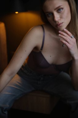 Siyah bir stüdyo ortamında poz veren mor takım elbiseli şık sarışın bir manken. Lüks kıyafet tanıtımı, karamsar yaşam tarzı fotoğrafçılığı ve şık moda trendleri..