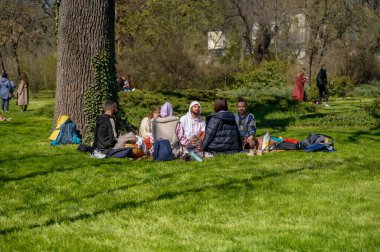 ODESSA, UKRAINE - 13 Nisan 2025: İnsanlar güneşli bir şehir parkında yeşil çimlerde oturup yoga ve meditasyon yapıyorlar. Sağlık kavramı, sağlıklı yaşam tarzı ve şehir ortamında huzur bulmak.