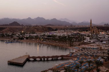 SHARM EL-SHEIKH, EGYPT - 11 Mart 2021: Aydınlatılmış tatil otelleri ve dağlarla deniz koyunun akşam manzarası. Bir tatil gezisi sırasında kıyı turizmi ve şehir gece hayatı kavramı