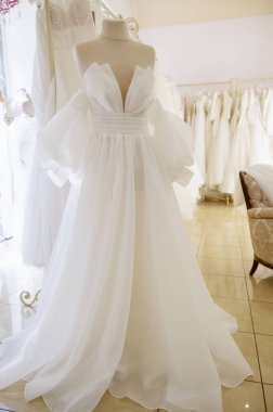 Şık ve zarif beyaz bir gelinlik bir sergi salonunun atmosferinde bir mankenin üzerinde sergileniyor. Yüksek kaliteli fotoğraf.