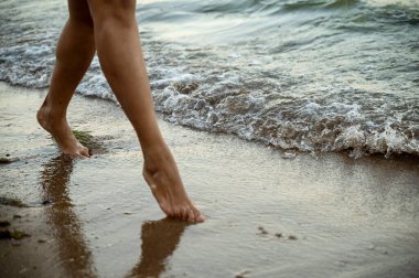 Bacak ayrıntıları ve alacakaranlıkta denizde duran siyah bir kadının siyah elbisesi. Gizem kavramı, kadınsı cazibe ve sahil kayaları tarafından huzurlu meditasyon.