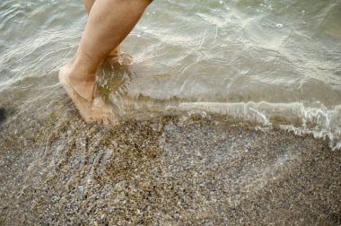 Deniz dalgalarının yanında ıslak kumda koşan Afrikalı bir Amerikalı kadının ayakları. Doğal çevrede kıyı sporları, yaz enerjisi ve ferahlatıcı fiziksel aktivite kavramı