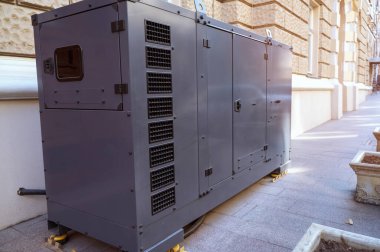Büyük endüstriyel dizel jeneratör şehrin kaldırımında bir binanın ön cephesinin yanında duruyor. Yedek güç kaynağı, enerji altyapısı ve kentsel elektrik bakımı kavramı