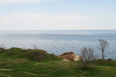 Geniş deniz manzarası güneşli bir bahar gününde yeşil çimenli bir uçurumdan görülüyor. Akdeniz atmosferi, huzurlu kıyı manzarası ve deniz ufku kavramı