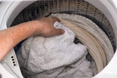 Kadın eli, çamaşır makinesinin varilinden ıslak çamaşırları çıkarıyor. Ev işi konsepti kumaş bakımını, ev temizlik rutinini, günlük ev hayatını gösteriyor.