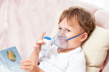 Boy making inhalation with a nebulizer at home and watching a book clipart