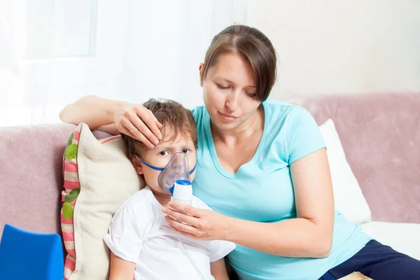 Jeune femme avec son fils faisant inhalation avec un nébuliseur à la maison et lire un livre — Photo