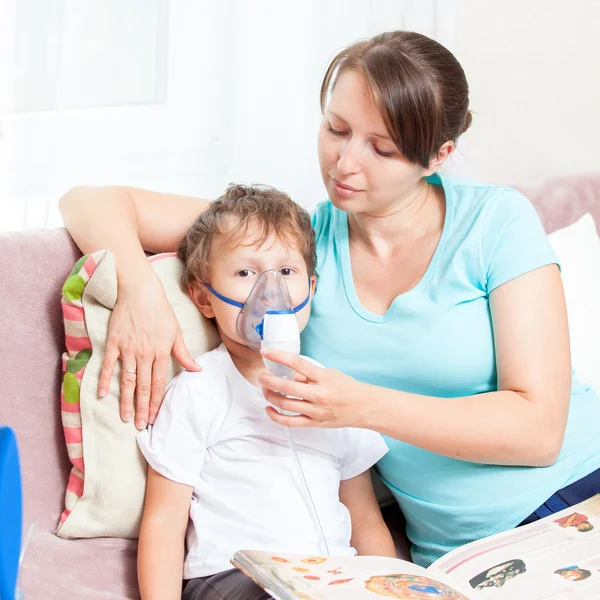 Jovem mulher com filho fazendo inalação com um nebulizador em casa e ler um livro — Fotografia de Stock