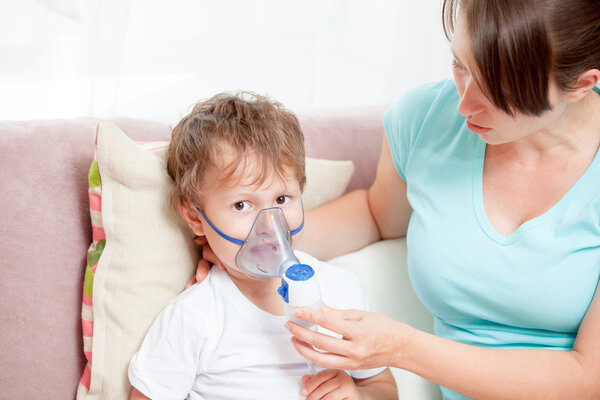 Молодая женщина с сыном делает вдох с распылителем в доме
