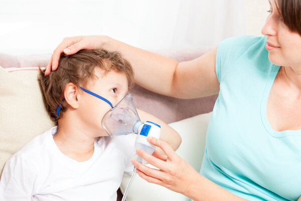 Молодая женщина с сыном делает вдох с распылителем в доме
