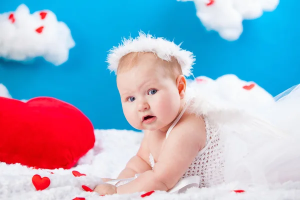 彼は赤いハートの周りに雲で横になっている翼と光輪、白いドレスの赤ちゃん天使 — ストック写真