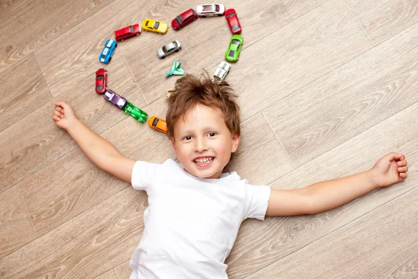 Ragazzo felice che gioca sul pavimento con auto giocattolo — Foto Stock