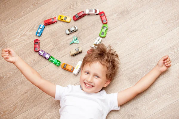 Ragazzo felice che gioca sul pavimento con auto giocattolo — Foto Stock