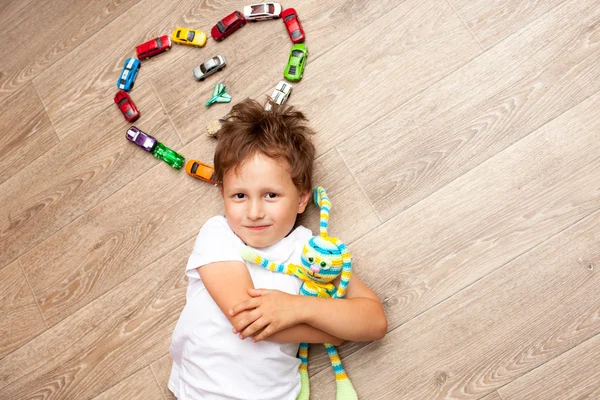 Menino feliz jogando no chão com carros de brinquedo — Fotografia de Stock
