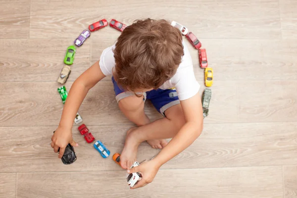 Ragazzo felice che gioca sul pavimento con auto giocattolo — Foto Stock