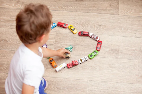 Ragazzo felice che gioca sul pavimento con auto giocattolo — Foto Stock