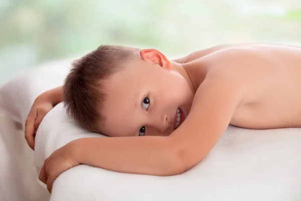 Niño feliz acostado en una mesa de masaje esperando un masaje —  Fotos de Stock