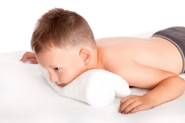 Niño feliz acostado en una mesa de masaje esperando un masaje —  Fotos de Stock