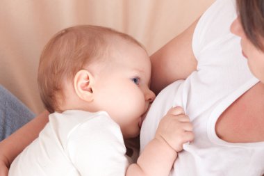 Genç bir kadın yatakta oturup bebeğin göğüs beslemeleri