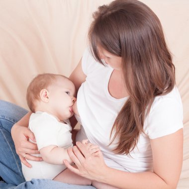 Genç bir kadın yatakta oturup bebeğin göğüs beslemeleri