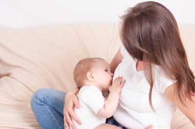 Genç bir kadın yatakta oturup bebeğin göğüs beslemeleri