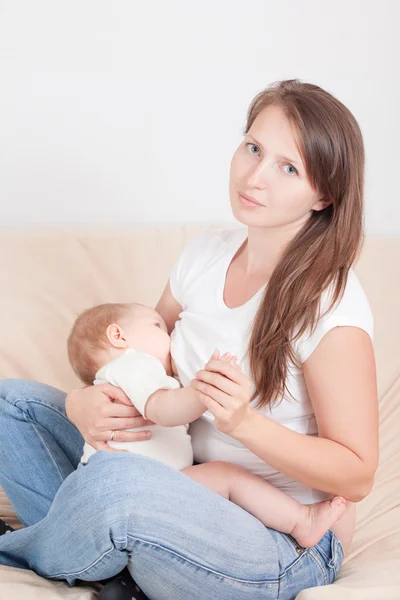 Μια νεαρή γυναίκα τροφές του μωρού στο στήθος, κάθεται στο κρεβάτι — Φωτογραφία Αρχείου