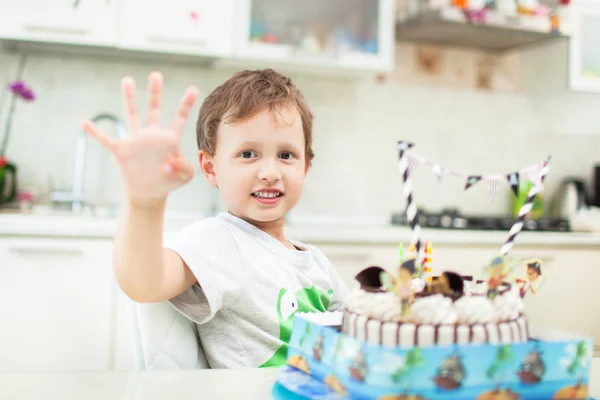 El chico se sienta con el pastel en la mesa y muestra la edad que tenía —  Fotos de Stock