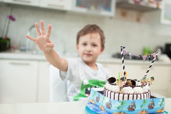 El chico se sienta con el pastel en la mesa y muestra la edad que tenía —  Fotos de Stock