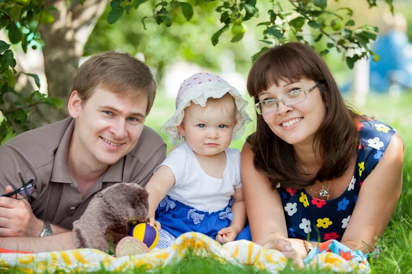 Молода щаслива сім'я сидить у парку на газоні — стокове фото