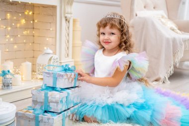 Mutlu Noeller ve tatiller! Süslü elbiseli şirin küçük kız ve taç hediyeleri açıyor. Hediye kutularıyla ağacın altındaki çocuklar. Noel oyuncaklarıyla dekore edilmiş oturma odası. Beyaz Saray 'da sıcak bir kış günü.