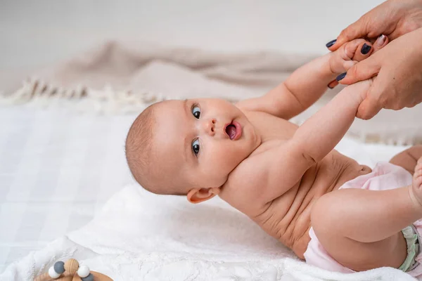 Cute baby sitting with support on bed. mother supports child sitting with her arms outstretched. child is just starting to sit on its own. the concept of developing new skills, support and care.