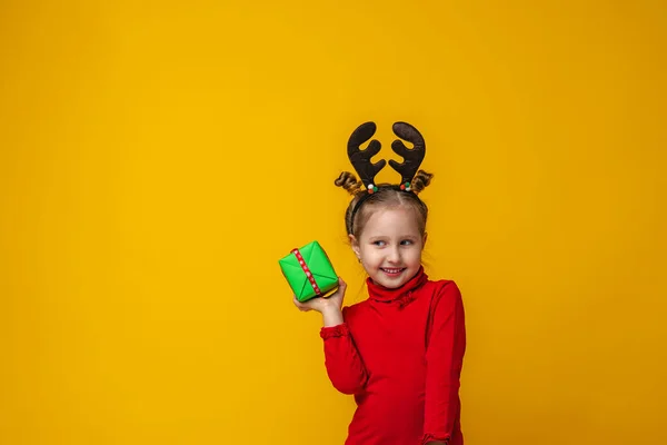 明るい黄色の背景にトナカイの角で幸せな女の子4歳 子供は幸せであり手に贈り物を持っています 新年の販売 コピースペース — ストック写真