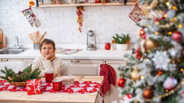 Mutlu Noeller ve mutlu Noeller! Noel arifesinde çocuk mutfakta Noel Baba 'nın hediyesini açıyor. Mutfak masasında hediye kutularıyla mutlu bir çocuk rüyasında Noel ağacına bakıyor..