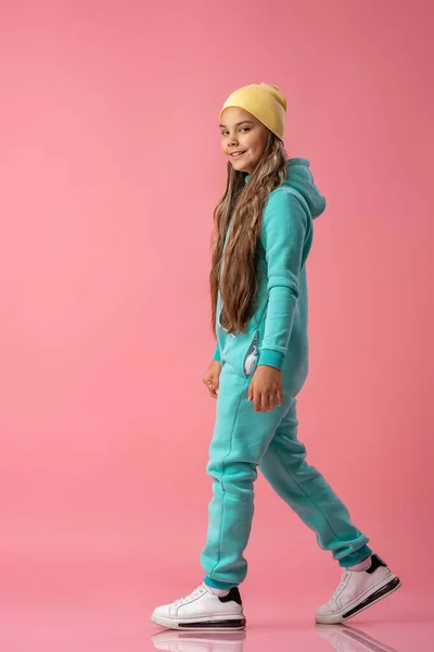 ビーニーのティーンの女の子 スニーカーのフードとターコイズ暖かいジャンプスーツはピンクの背景スタジオに行きます 冬と秋の子供服 快適な子供服 スペースのコピー — ストック写真