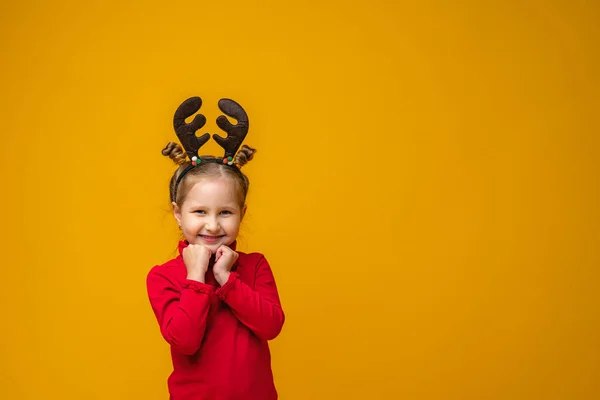 快乐的小女孩4岁在一个明亮的黄色背景驯鹿鹿角 那孩子高兴极了 双手紧握着下巴 新年的销售 复制空间 — 图库照片