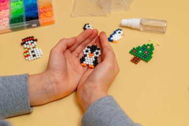 Çocuk, taşaklardan yapılmış bir penguen oyuncağı tutuyor. Kendi elleriyle yapmış. Yakın plan. El yapımı çocuk eli, el yapımı mozaik, seçici odaklanma. Yeni yıl ve Noel konsepti