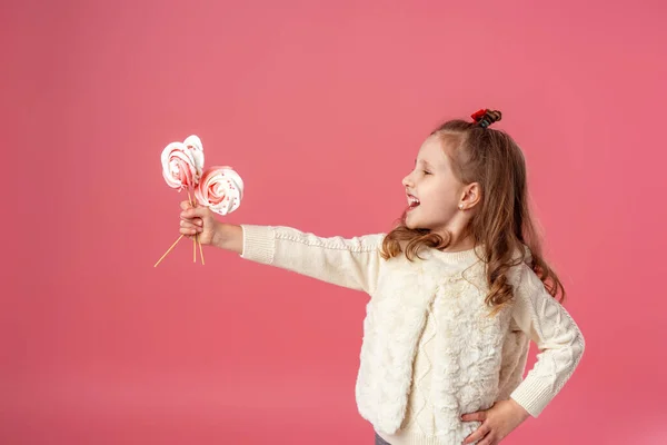 快乐的小女孩牵着她的手 在粉色背景的手杖上拿出3块白色和粉色的蛋白糖 那孩子笑了 想吃糖果 复制空间 — 图库照片