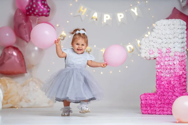 First year\'s birthday. happy little girl in white dress run in background with garlands and pink balloons, celebrating her first birthday. Decoration birthday. copy space.