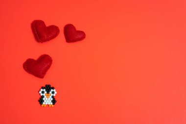 Taşaklardan yapılmış bir penguen figürü ve kırmızı arka planda keçeden yapılmış bir kalp. El yapımı çocuk eli, el yapımı su mozaiği, seçici odaklanma. Sevgililer Günü konsepti