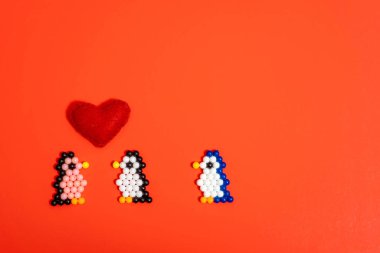 Taşaklardan yapılmış bir penguen figürü ve kırmızı arka planda bulunan bir kalp. El yapımı çocuk eli, el yapımı su mozaiği, seçici odaklanma. Sevgililer Günü konsepti