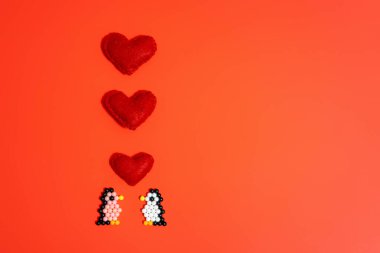 Taşaklardan yapılmış bir penguen figürü ve kırmızı arka planda bulunan bir kalp. El yapımı çocuk eli, el yapımı su mozaiği, seçici odaklanma. Sevgililer Günü konsepti